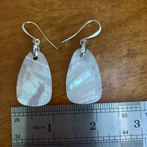 May include: A pair of white iridescent shell earrings with silver hooks. The earrings are approximately 1 inch long.