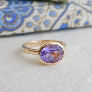 May include: A gold ring with a bezel setting featuring a large oval amethyst gemstone.