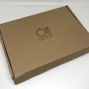 May include: A brown cardboard box with the text "OH OLIVER" printed in black. The box is rectangular and has a simple, clean design. The logo features a circle and a stylized "H".