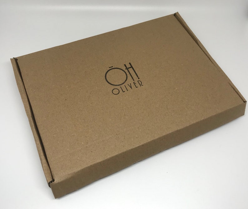 May include: A brown cardboard box with the text "OH OLIVER" printed in black. The box is rectangular and has a simple, clean design. The logo features a circle and a stylized "H".