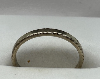 May include: A silver ring with a textured, rope-like design around the band. The ring is set against a white background, highlighting its intricate details. The ring appears to be a wedding band or a simple, elegant piece of jewelry.
