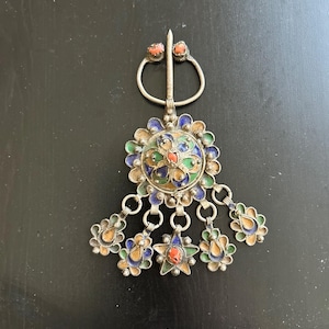 May include: A silver-toned brooch with a central floral design, featuring colorful enamel and coral-colored accents. The brooch has a pin closure and dangling floral charms.