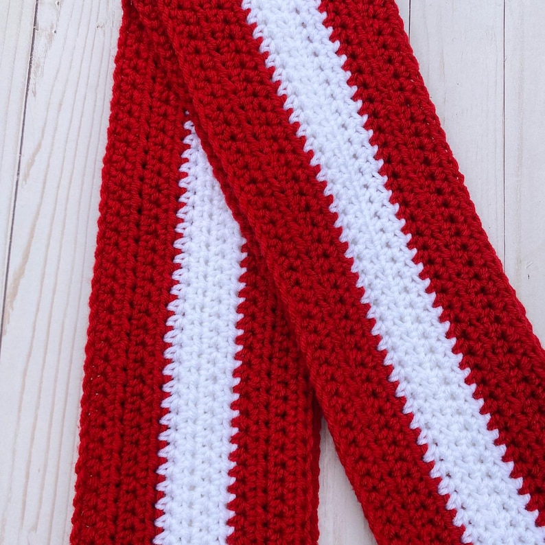 Red and white striped crocheted scarf folded in half and laid at an angle.  Stripes run lengthwise on the scarf.  There are two red stripes on the outside lengths of the scarf, and the center stripe is white.