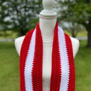 Red and white striped crocheted scarf draped around the neck of a mannequin.  Stripes run lengthwise on the scarf.  There are two red stripes on the outside lengths of the scarf, and the center stripe is white.