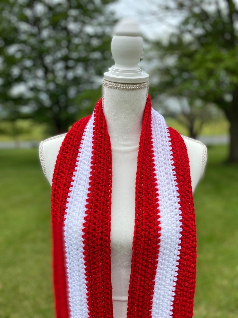 Red and white striped crocheted scarf draped around the neck of a mannequin.  Stripes run lengthwise on the scarf.  There are two red stripes on the outside lengths of the scarf, and the center stripe is white.