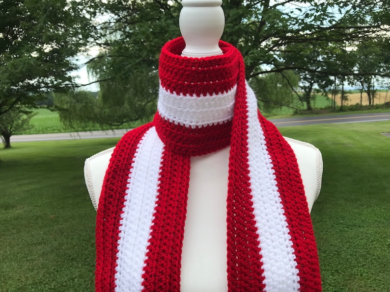 Red and white striped crocheted scarf draped around the neck of a mannequin.  Stripes run lengthwise on the scarf.  There are two red stripes on the outside lengths of the scarf, and the center stripe is white.