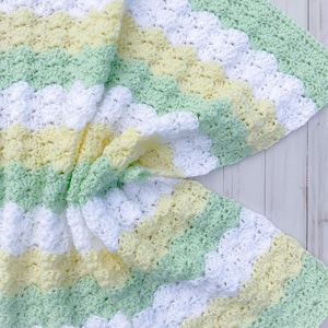 May include: A crocheted baby blanket with a chevron pattern in white, yellow, and green.