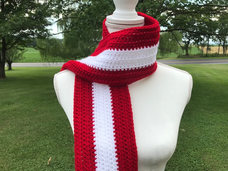 Red and white striped crocheted scarf draped around the neck of a mannequin.  Stripes run lengthwise on the scarf.  There are two red stripes on the outside lengths of the scarf, and the center stripe is white.