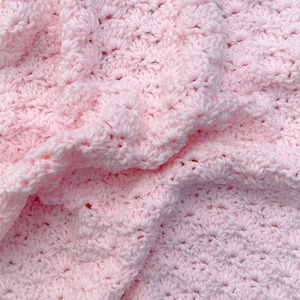 Light pink baby blanket crocheted in a shell stitch which gives it a wonderful texture.  Edges are straight with no border.  Picture taken on a white wooden background.  Picture is of the blanket gathered into a pile to show softness.