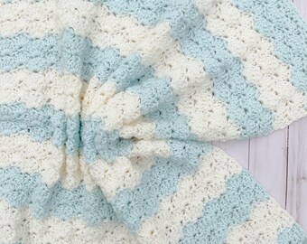 May include: A crocheted baby blanket with a striped pattern in white and light blue.