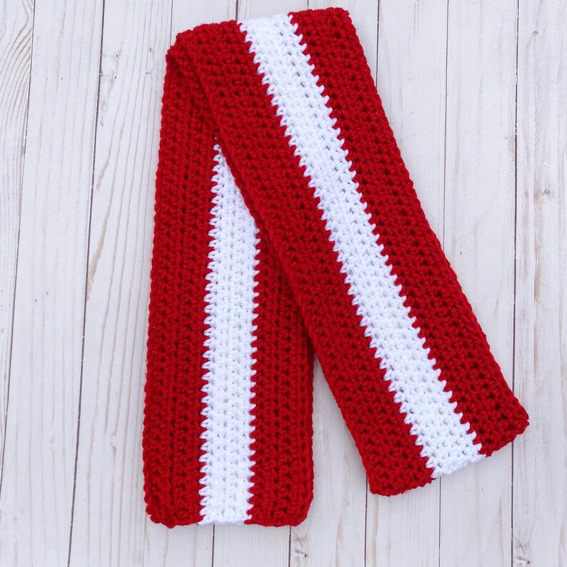 Red and white striped crocheted scarf laid flat and folded in half.  Stripes run lengthwise on the scarf.  There are two red stripes on the outside lengths of the scarf, and the center stripe is white.