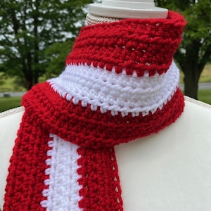 Red and white striped crocheted scarf draped around the neck of a mannequin.  Stripes run lengthwise on the scarf.  There are two red stripes on the outside lengths of the scarf, and the center stripe is white.