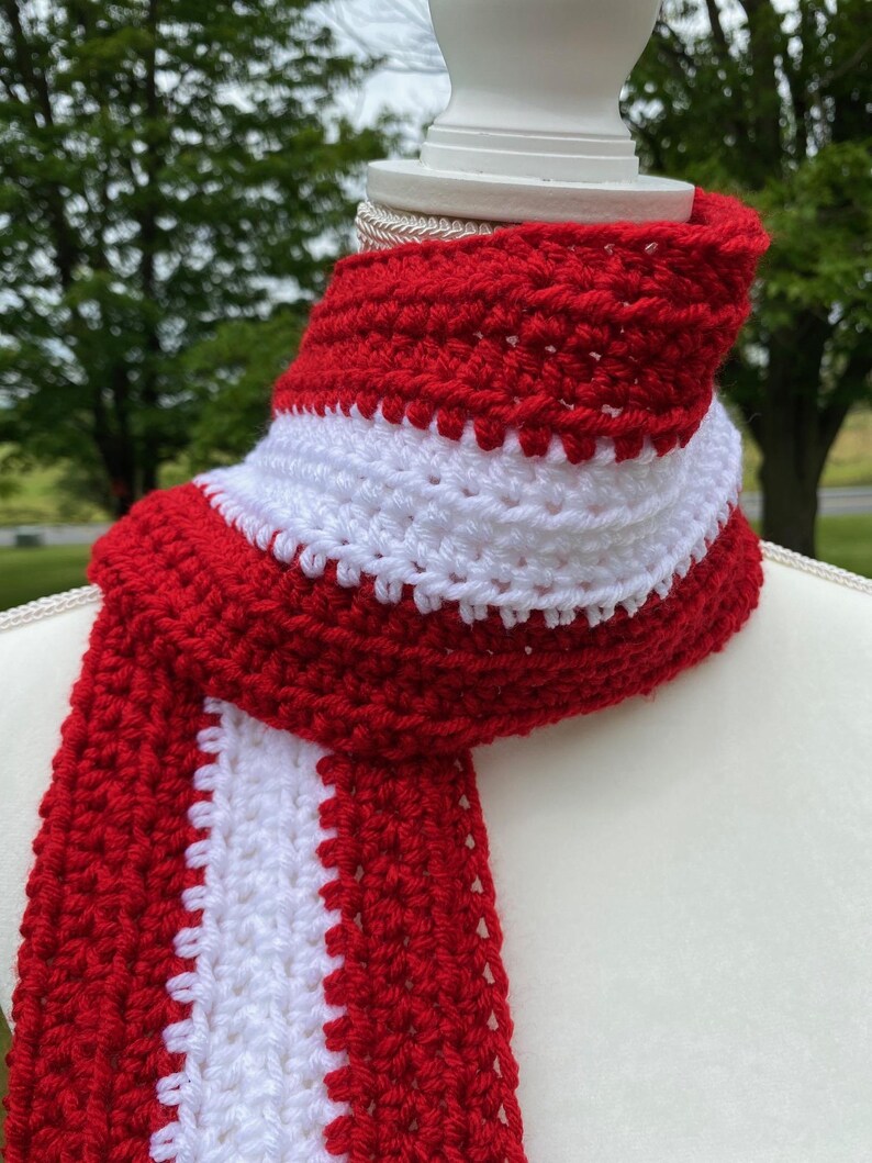 Red and white striped crocheted scarf draped around the neck of a mannequin.  Stripes run lengthwise on the scarf.  There are two red stripes on the outside lengths of the scarf, and the center stripe is white.
