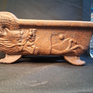 May include: A rectangular, brown ceramic planter with a textured surface. The planter features detailed relief carvings of a dragon and fish. It rests on four small feet and is suitable for small plants or succulents.