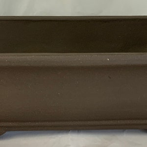 May include: A rectangular brown ceramic bonsai pot with a square base and rounded edges.