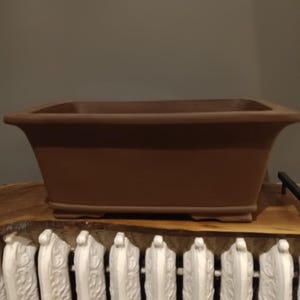 May include: A brown rectangular ceramic bonsai pot with a slightly flared rim and a flat base.