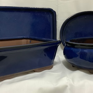 Może przedstawiać: Trzy niebieskie ceramiczne doniczki do bonsai. Jedna doniczka prostokątna z dopasowaną pokrywką, jedna doniczka owalna z dopasowaną pokrywką i jedna doniczka prostokątna bez pokrywki.