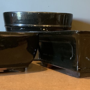 Może przedstawiać: Trzy czarne ceramiczne doniczki do bonsai o różnych rozmiarach i kształtach. Doniczki są wszystkie szkliwione i mają błyszczące wykończenie.