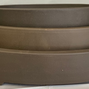 May include: Three brown ceramic oval planters stacked on top of each other. The planters are unglazed and have a rough texture.