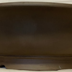 May include: A brown ceramic bonsai pot with a wide, shallow base and a rounded, oval shape.