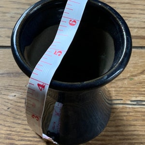 May include: A dark blue ceramic vase with a wide opening and a narrow base. A white measuring tape is wrapped around the vase, with the numbers 3, 4, 5, 6, 7, 8, and 9 visible.