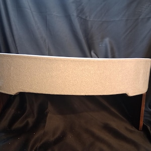May include: A wide, shallow, off-white ceramic bonsai pot featuring a distinct crackle glaze finish. The vessel is supported by two dark brown wooden legs that elevate the base, creating a clear gap between the pot and the surface below.