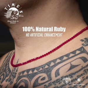 Könnte beinhalten: Nahaufnahme eines Halses, an dem eine Halskette aus roten Rubinperlen getragen wird. Die Halskette besteht aus kleinen, facettierten Perlen und wird von einer Person mit einem Tattoo getragen. Der Text "100% Natural Ruby" und "NO ARTIFICIAL ENHANCEMENT" ist auf dem Bild zu sehen.
