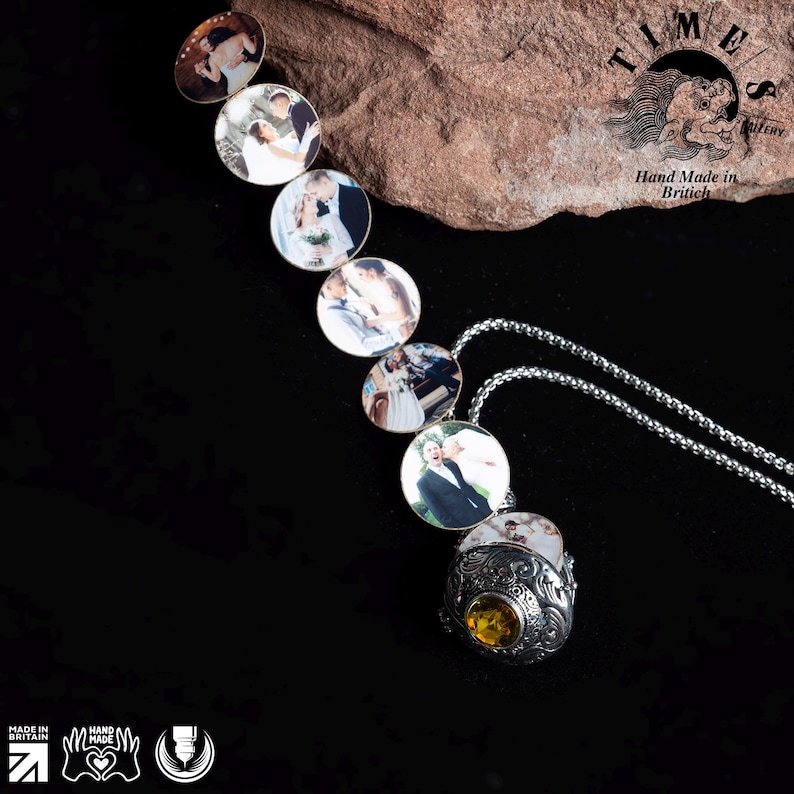 May include: A silver locket necklace with a round, ornate pendant. The pendant has a small, yellow gemstone in the center and is surrounded by a detailed design. The necklace is made up of multiple round lockets, each containing a different photo of a couple. The lockets are connected by a silver chain. The necklace is displayed on a brown, textured surface. The text "TIMES" is visible in the background.