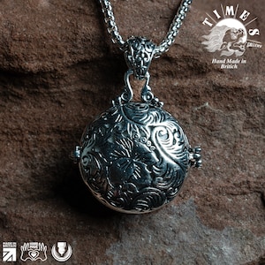 May include: A silver pendant necklace with a round, ornate locket featuring a floral design. The locket is attached to a silver chain.