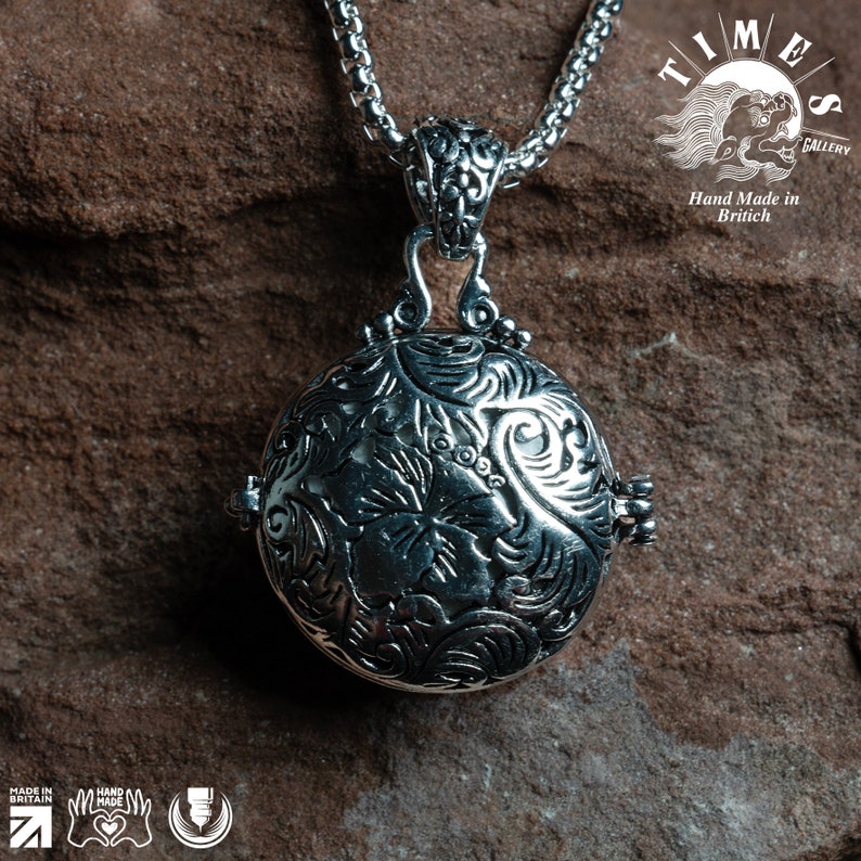 May include: A silver pendant necklace with a round, ornate locket featuring a floral design. The locket is attached to a silver chain.