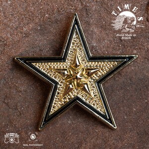 May include: A gold five-pointed star with black outlines. The star has a textured surface and is a decorative piece. The text "TIMES GALLERY" and "Hand Made in Britain" is visible in the background.