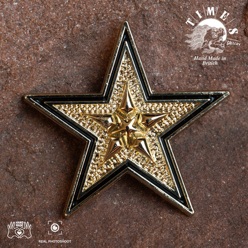 May include: A gold five-pointed star with black outlines. The star has a textured surface and is a decorative piece. The text "TIMES GALLERY" and "Hand Made in Britain" is visible in the background.