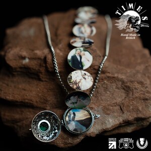 May include: A silver locket necklace with a series of smaller lockets, each containing a photo of a couple. The larger locket is open, revealing a photo of a couple on a beach. The necklace is on a brown rock with the text "TIMES GALLERY Hand Made in British" in the background.