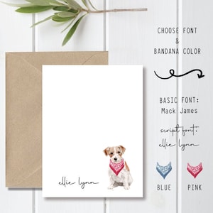 May include: A white card with a watercolor illustration of a dog wearing a pink bandana. The text "ellie lynn" is written in cursive at the bottom of the card. The card is on a white wooden surface with a brown envelope and a pencil.