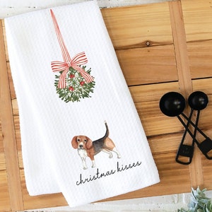 May include: White kitchen towel with a red and white striped Christmas wreath and a beagle dog illustration. The text "christmas kisses" is printed below the dog.