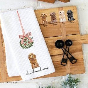 May include: White kitchen towel with a red and white striped ribbon and a green wreath with red berries. The towel also features a brown doodle of a dog and the text "christmas kisses".