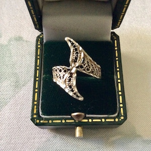 Op de afbeelding: Een zilveren filigraanring met een delicaat, ingewikkeld ontwerp. De ring wordt gepresenteerd in een groene fluwelen ringdoos.