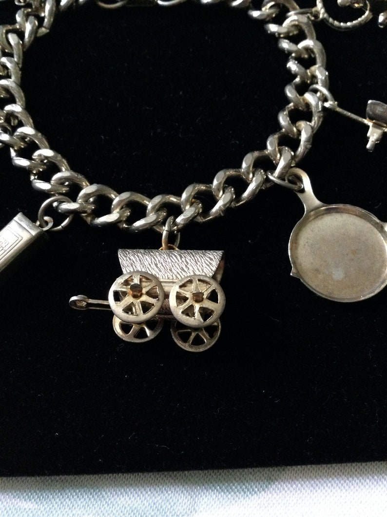 Pode incluir: Um bracelete de prata com uma variedade de pingentes, incluindo um carrinho de beb&ecirc;, uma frigideira e um pequeno livro. O bracelete &eacute; feito de uma corrente grossa e robusta.