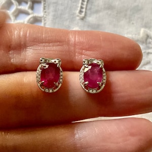 Peut inclure: Une paire de boucles d'oreilles en argent avec une pierre ovale rouge entourée de petites pierres blanches. Les boucles d'oreilles ont un design en forme de nœud.