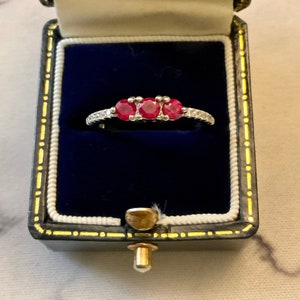 Op de afbeelding: Een zilveren ring met drie rode edelstenen en een band van kleine diamanten.