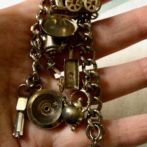 Pode incluir: Um bracelete de prata com uma variedade de pingentes, incluindo um bule, um sino, uma carro&ccedil;a e uma pequena frigideira.