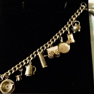 Pode incluir: Um bracelete de prata com uma variedade de pingentes, incluindo um bule de ch&aacute;, uma carro&ccedil;a, uma panela e uma cafeteira.