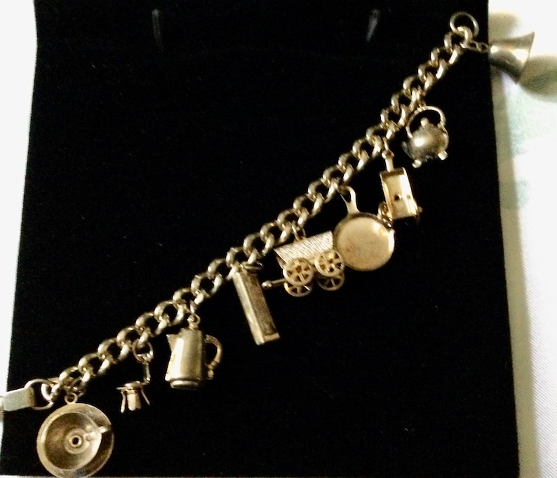 Pode incluir: Um bracelete de prata com uma variedade de pingentes, incluindo um bule de ch&aacute;, uma carro&ccedil;a, uma panela e uma cafeteira.