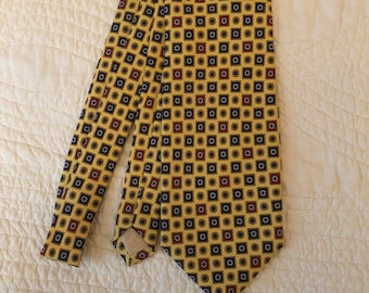 May include: A yellow patterned necktie with a repeating pattern of small squares and circles. The tie has a dark blue and red color scheme.