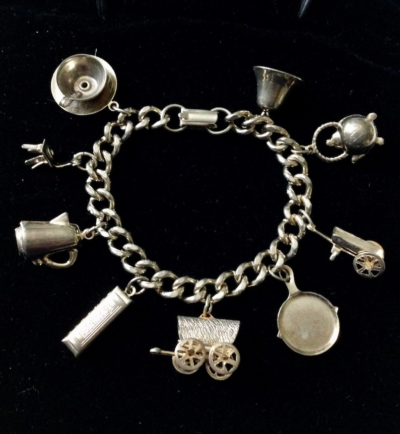 Pode incluir: Um bracelete de prata com uma variedade de pingentes, incluindo um bule de ch&aacute;, uma cafeteira, uma carro&ccedil;a, uma frigideira, um hidrante, um sino e uma x&iacute;cara. O bracelete &eacute; feito de uma corrente de prata.