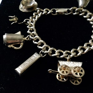 Pode incluir: Um bracelete de prata com v&aacute;rios pingentes, incluindo uma ch&aacute;vena de ch&aacute;, uma cafeteira, uma caixa de m&uacute;sica e uma carruagem. O bracelete &eacute; feito de uma corrente de prata.