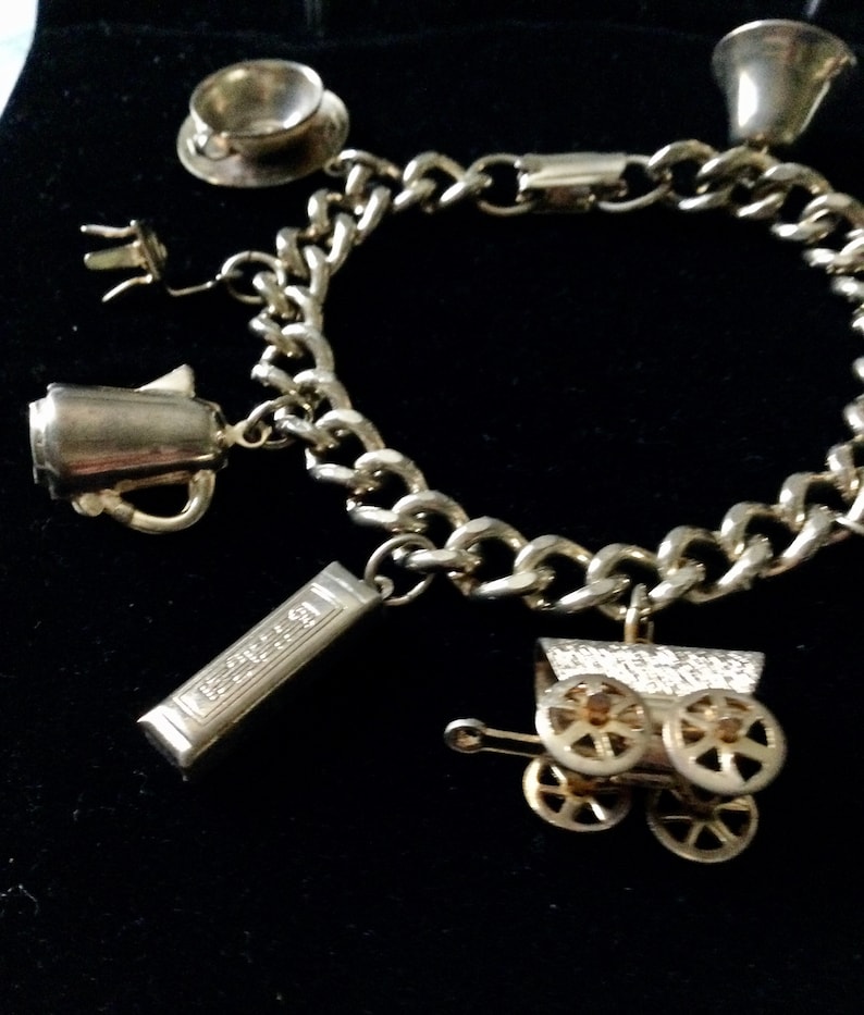 Pode incluir: Um bracelete de prata com v&aacute;rios pingentes, incluindo uma ch&aacute;vena de ch&aacute;, uma cafeteira, uma caixa de m&uacute;sica e uma carruagem. O bracelete &eacute; feito de uma corrente de prata.
