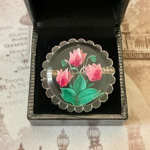 Peut inclure: Une broche vintage en forme de fleurs roses et vertes dans un dôme en verre transparent. La broche est dans un écrin en velours noir.