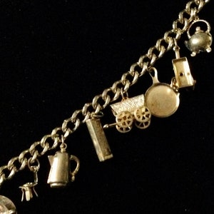 Pode incluir: Um bracelete de ouro com v&aacute;rios pingentes, incluindo um bule, uma carro&ccedil;a, uma frigideira, uma caixa de f&oacute;sforos e um jarro.
