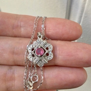 May include: A silver chain necklace with a pendant featuring a pink gemstone surrounded by smaller clear gemstones in a delicate, intricate design.